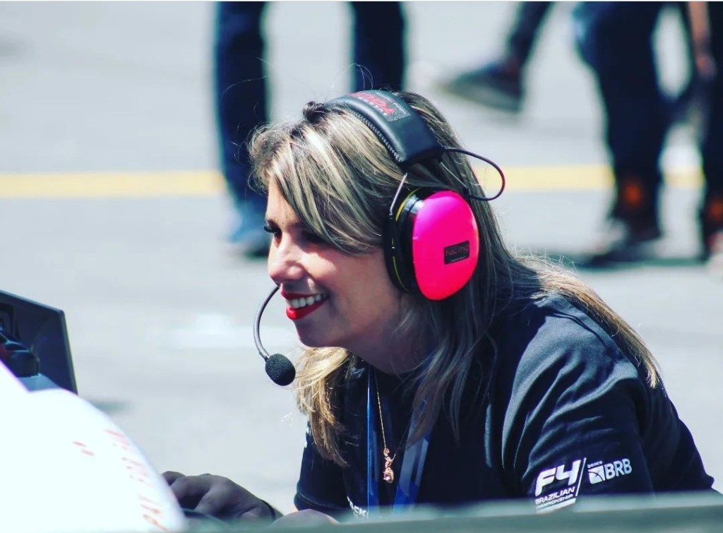 Mulher de cabelos loiros e batom vermelho utilizando fone de ouvido rosa. 