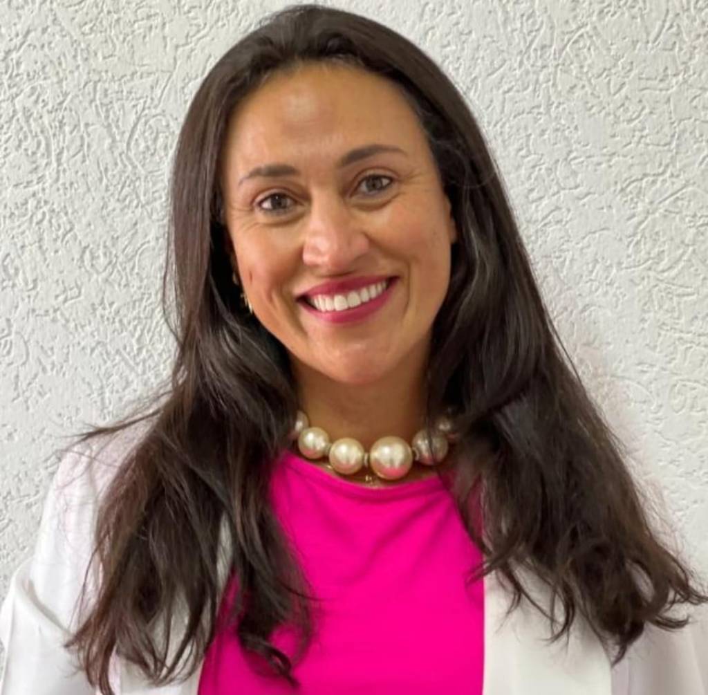 Mulher sorrindo com camiseta rosa e blusa branca.