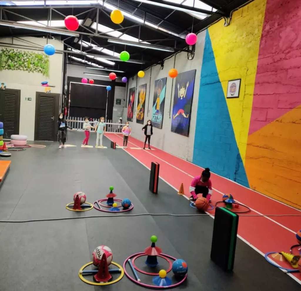 Crianças pulando e brincando com bolas e bambolês de diversas cores. 