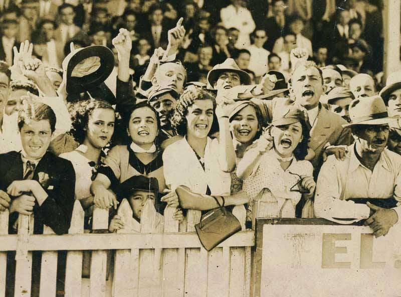 Imagem preto e branca da torcida uniformizada do cambuci composta por homens, mulheres e crianças vestidas de roupas típicas dos anos 30